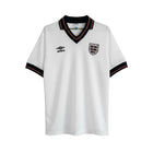Camiseta de fútbol retro blanca de manga corta de Umbro para Inglaterra 1984, con cuello en V negro y ribete rojo, y escudo del equipo bordado.